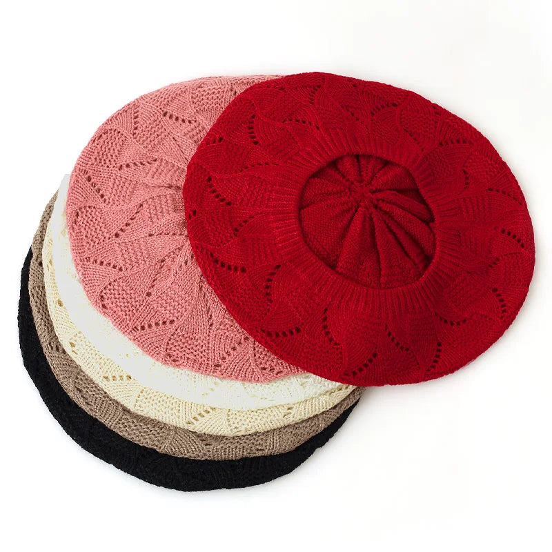 Stack of knit berets in red, pink, beige, and black on a white background