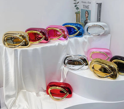 Colourful clutch bags displayed on a white stand with a magazine and plant in the background.