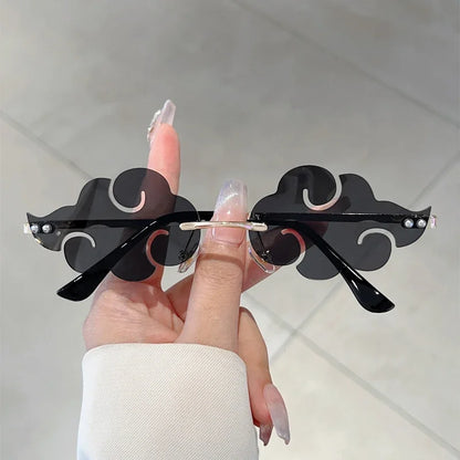 Black cloud-shaped sunglasses held by a hand against a neutral background