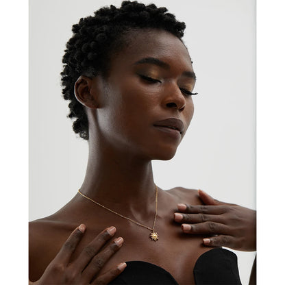 Woman wearing a gold necklace with a star design on a plain background