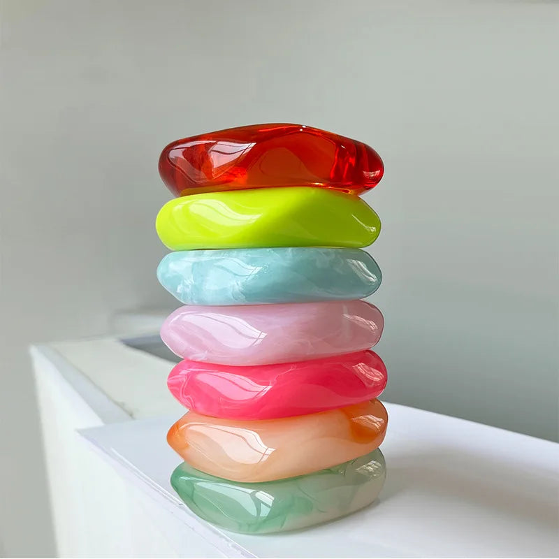 Stack of colourful resin bangles on a white surface with a light grey background