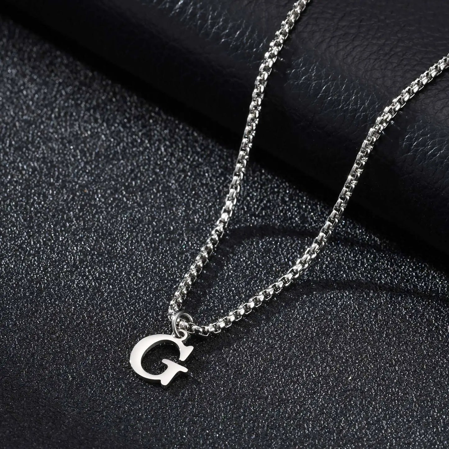 Silver necklace with a 'G' pendant on a black textured surface