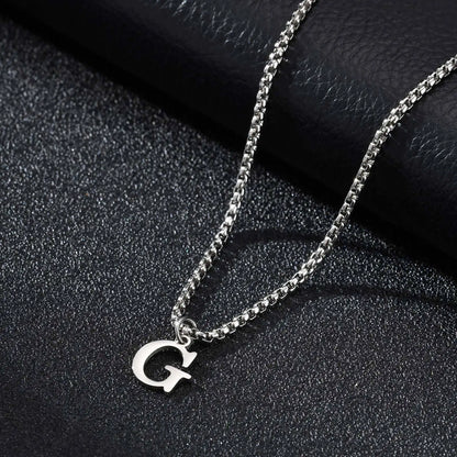 Silver necklace with a 'G' pendant on a black textured surface