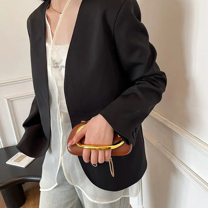 Person wearing a black blazer and holding a brown clutch in an indoor setting.