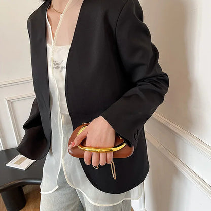 Person wearing a black blazer and holding a brown clutch in an indoor setting.