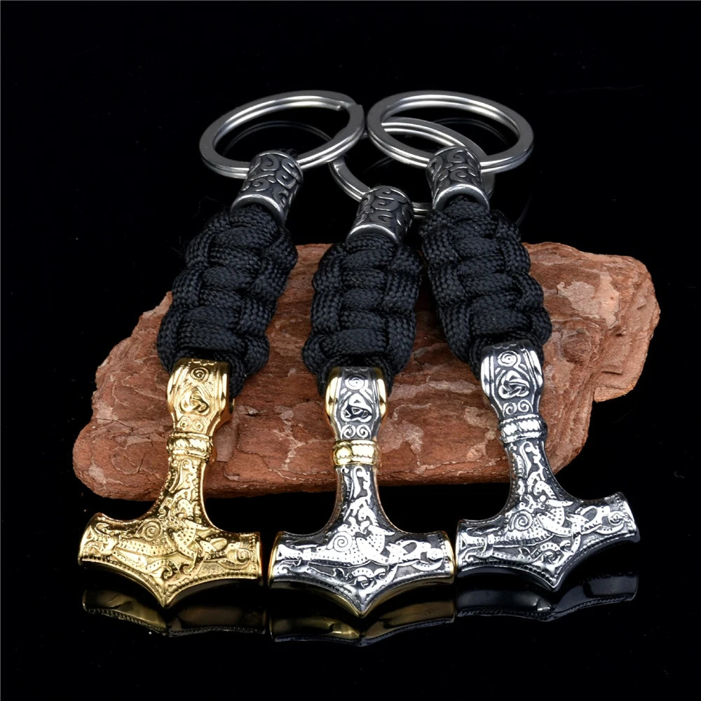 Three Thor's hammer keychains in gold, silver, and bronze on a dark background.