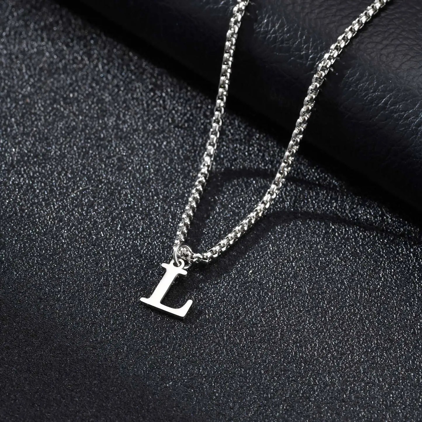 Silver necklace with a 'L' pendant on a dark textured surface