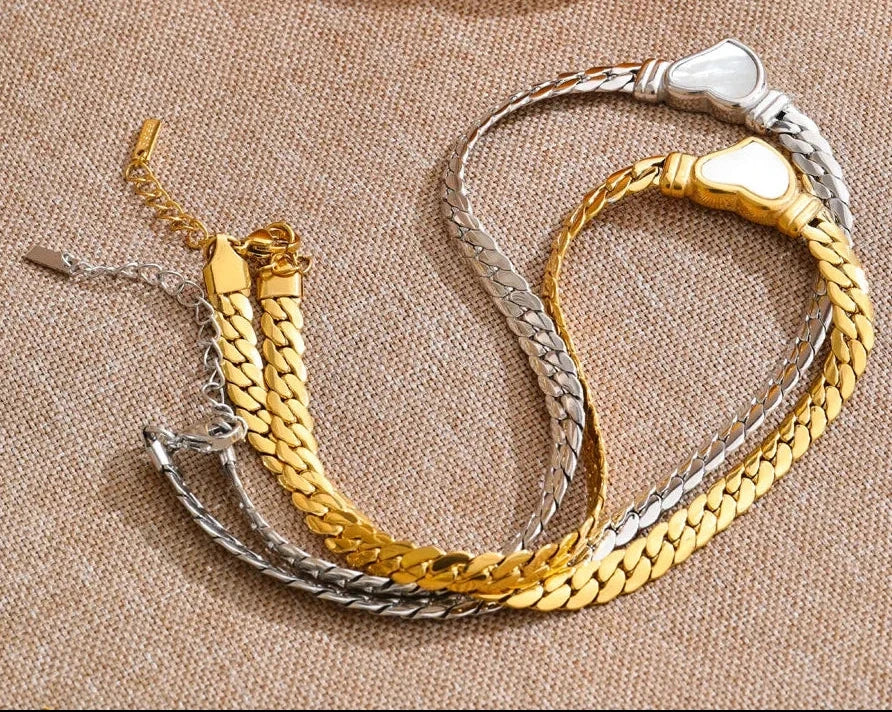 Three gold and silver bracelets on a textured surface with a yellow pepper in the background.