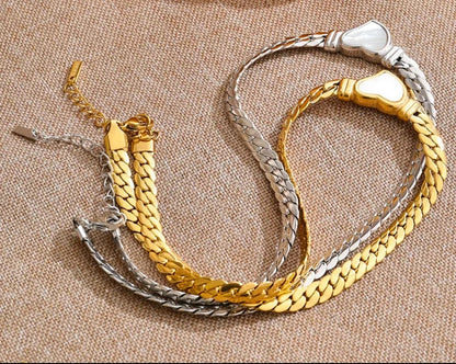 Three gold and silver bracelets on a textured surface with a yellow pepper in the background.