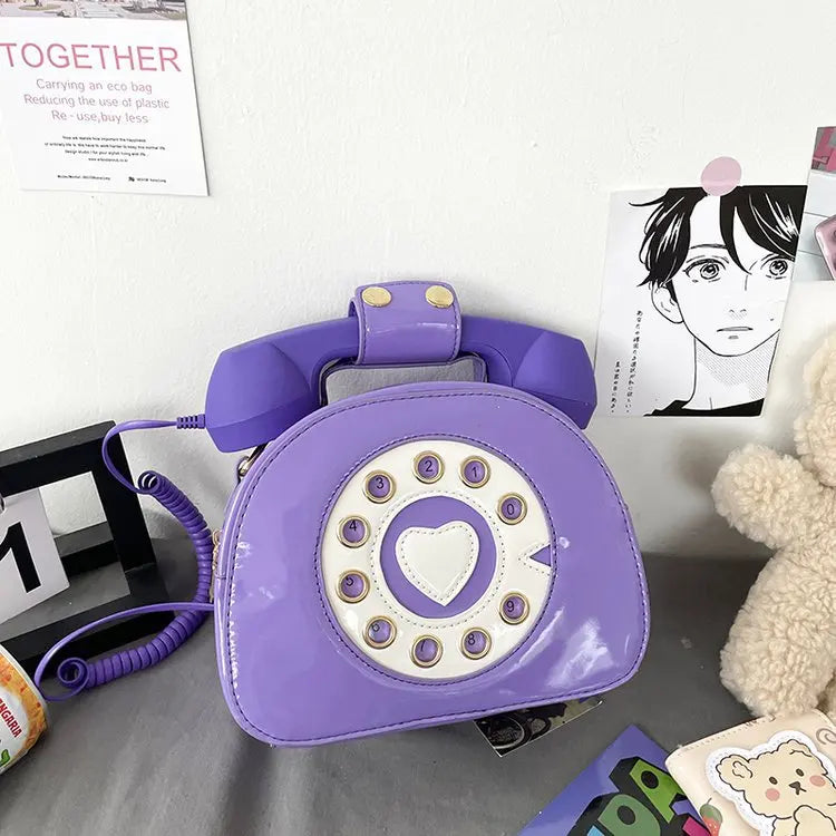 Purple phone-shaped bag with a heart design on a surface with various items.