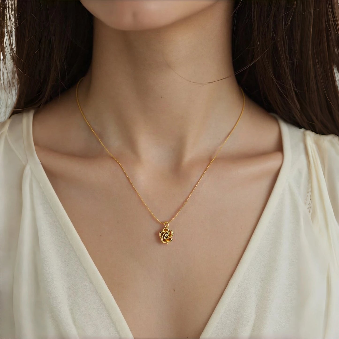 Gold necklace with a floral pendant worn by a person in a white top.