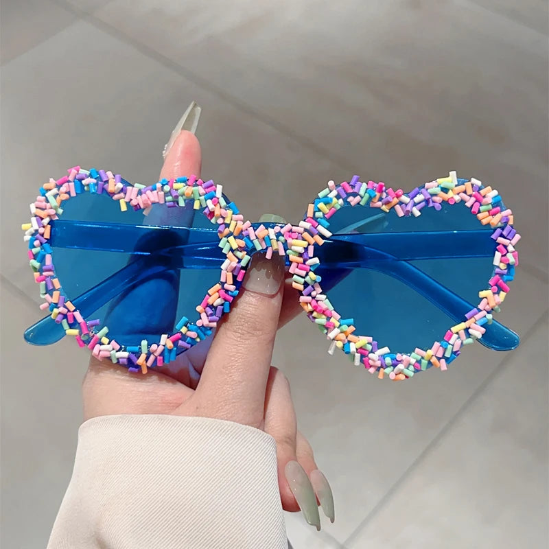 Blue sunglasses with colourful bead embellishments held by a hand against a neutral background