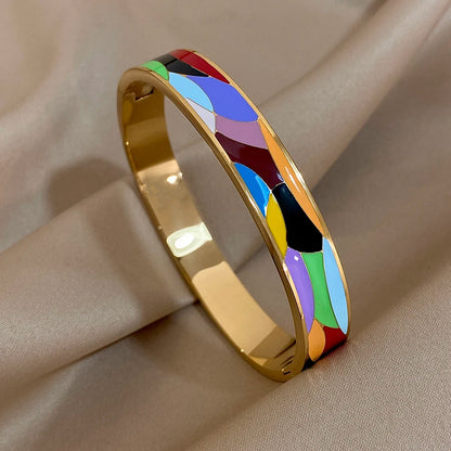 Gold bangle with colourful inlay on a beige fabric background