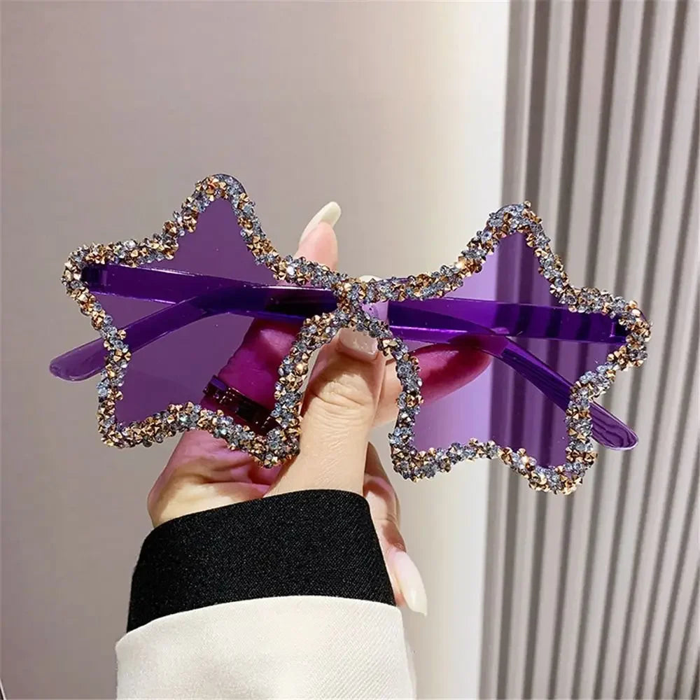 Star-shaped sunglasses with purple frame and rhinestone details held by a hand.