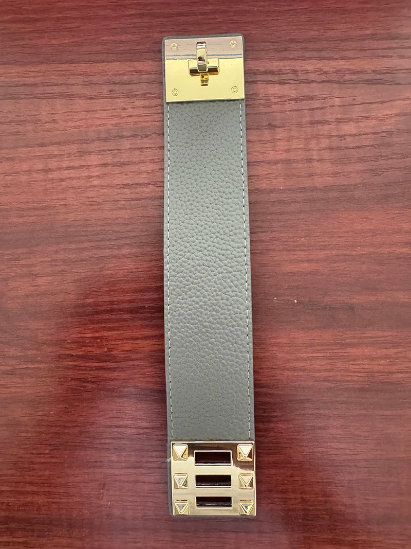 Grey leather strap with gold hardware on a wooden surface