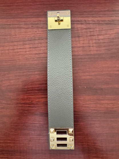 Grey leather strap with gold hardware on a wooden surface