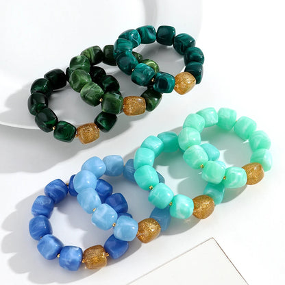 Three beaded bracelets in green, blue, and turquoise on a white surface.