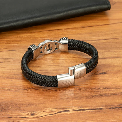 Black braided leather bracelet with silver clasp on a wooden surface