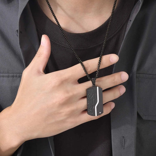 Person holding a black dog tag necklace with a silver stripe design.