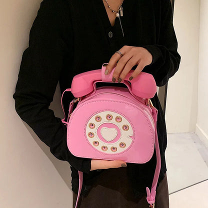 Person holding a pink phone-shaped handbag with a heart design.