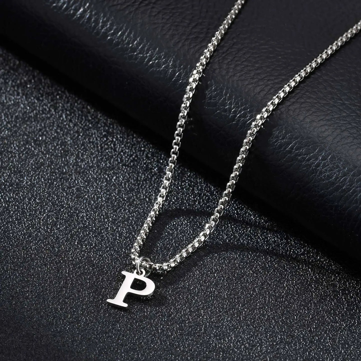 Silver necklace with a 'P' pendant on a dark textured surface