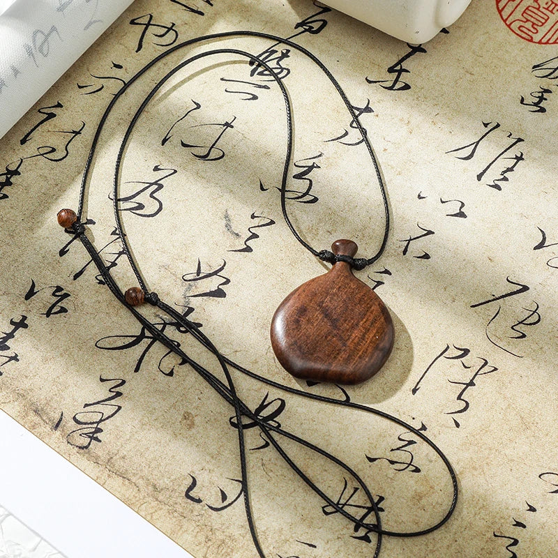 Wooden pendant necklace on a textured surface with calligraphy