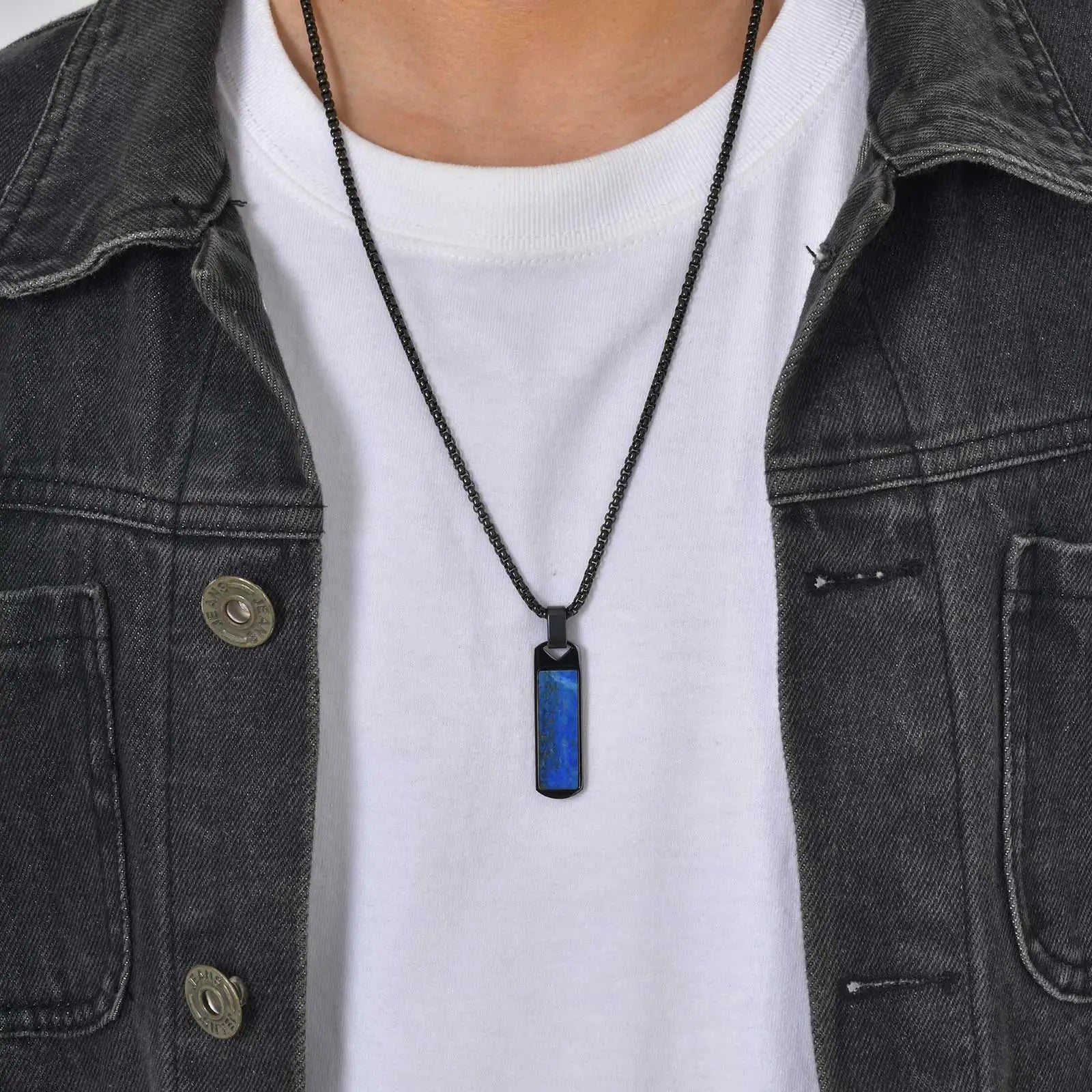 Person wearing a black necklace with a blue pendant on a plain background