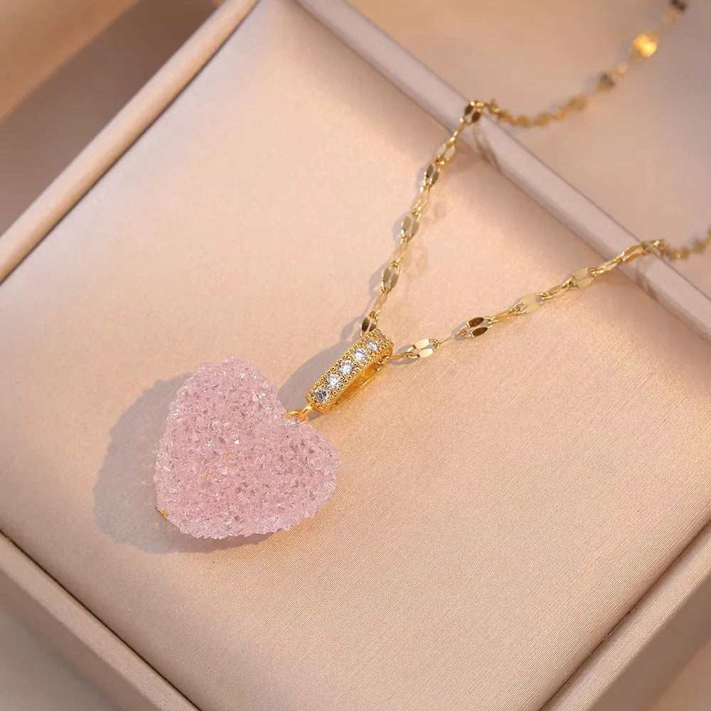 Gold necklace with a pink heart-shaped pendant on a beige jewelry box