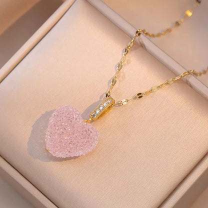 Gold necklace with a pink heart-shaped pendant on a beige jewelry box