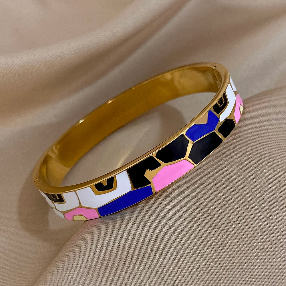 Gold bangle with colourful geometric pattern on a beige fabric background
