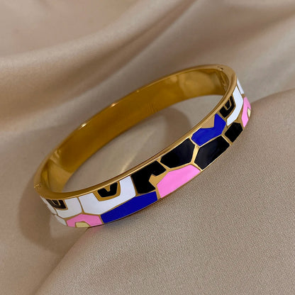 Gold bangle with colourful geometric pattern on a beige fabric background