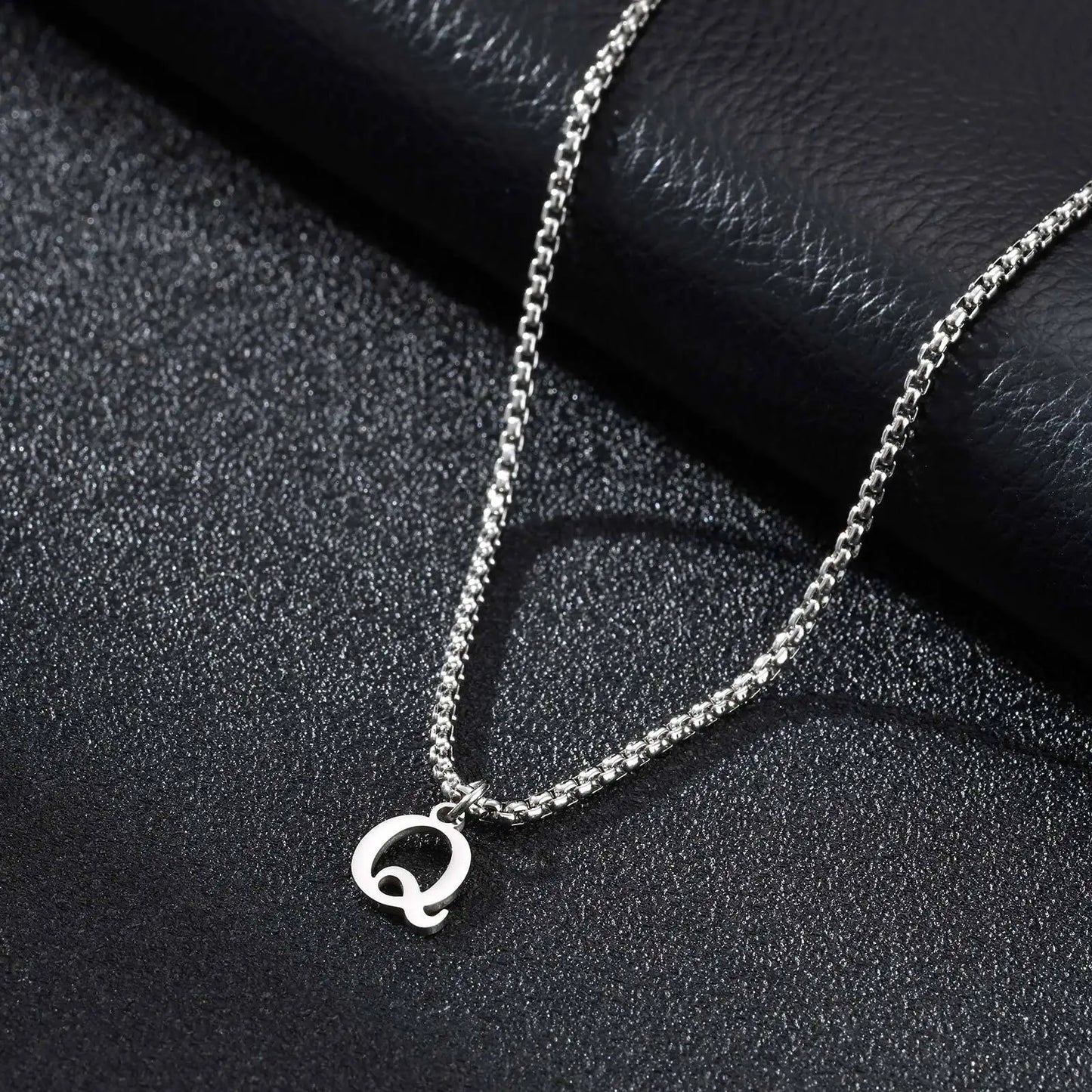 Silver necklace with a 'Q' pendant on a black textured surface