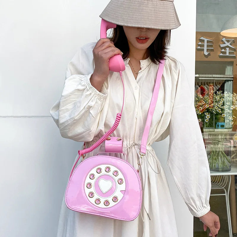 Person holding a pink phone-shaped handbag with a coiled cord, wearing a white dress.