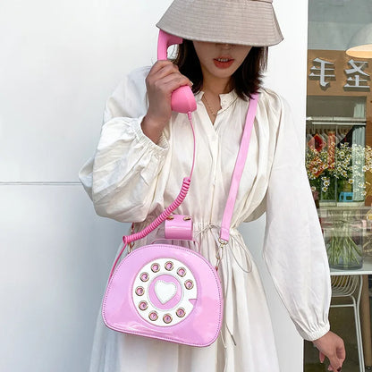 Person holding a pink phone-shaped handbag with a coiled cord, wearing a white dress.
