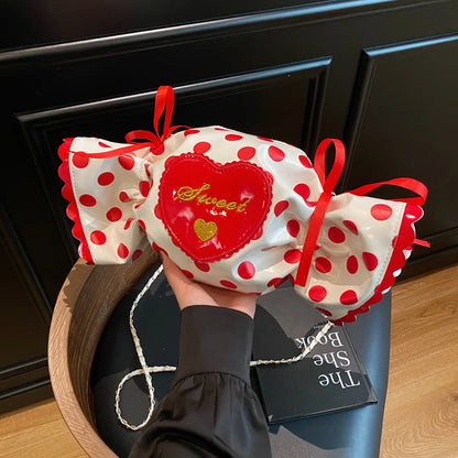 Polka dot candy-shaped bag with red bows held by a person against a dark background.