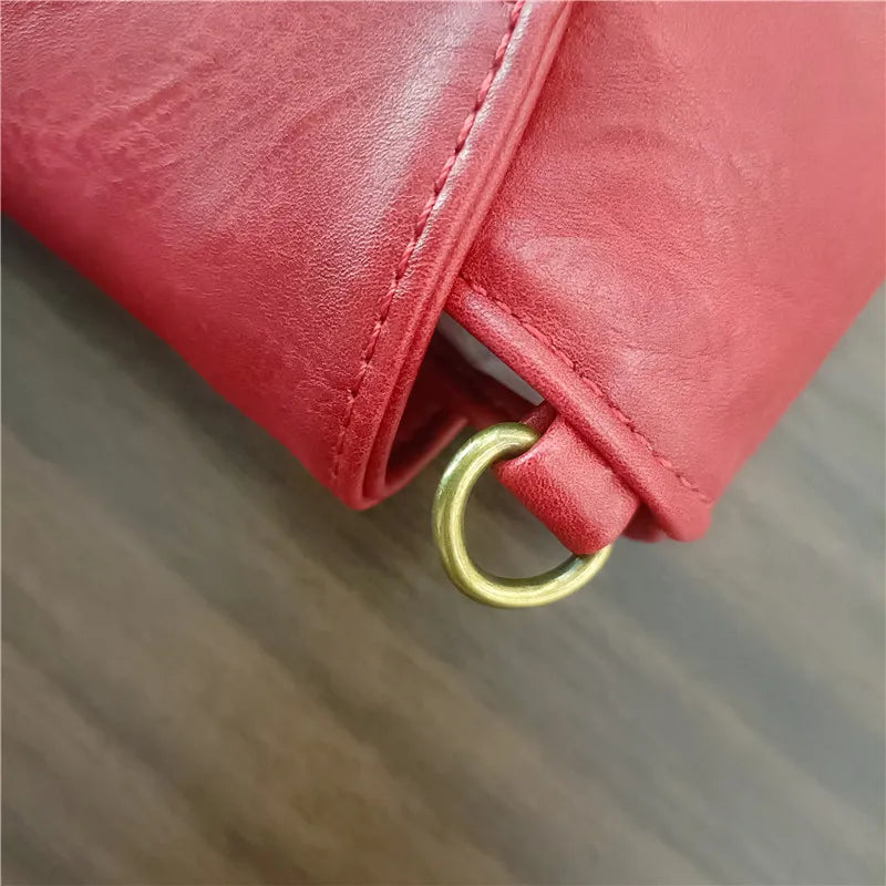 Close-up of a red leather bag with a gold ring handle on a wooden surface.
