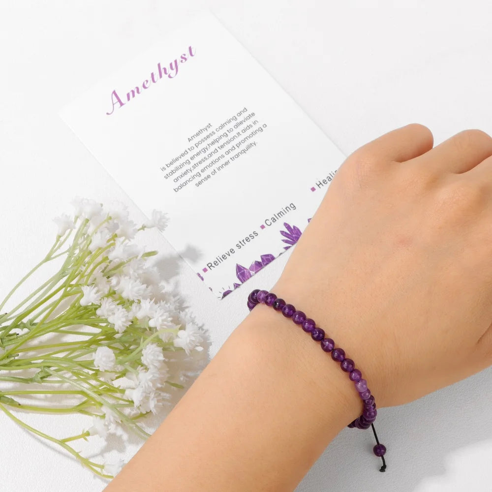 Hand wearing a purple beaded bracelet with white flowers and an open book in the background