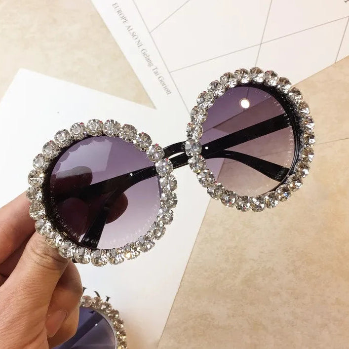 Sunglasses with decorative frame held by a hand on a light background