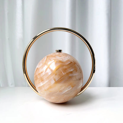 Clutch bag with a spherical beige center and gold circular frame on a grey background.