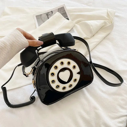 Black rotary phone-shaped handbag with a heart detail on a white surface