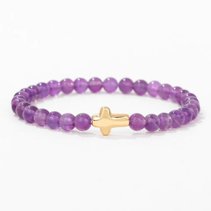 Purple beaded bracelet with a gold cross charm on a white background