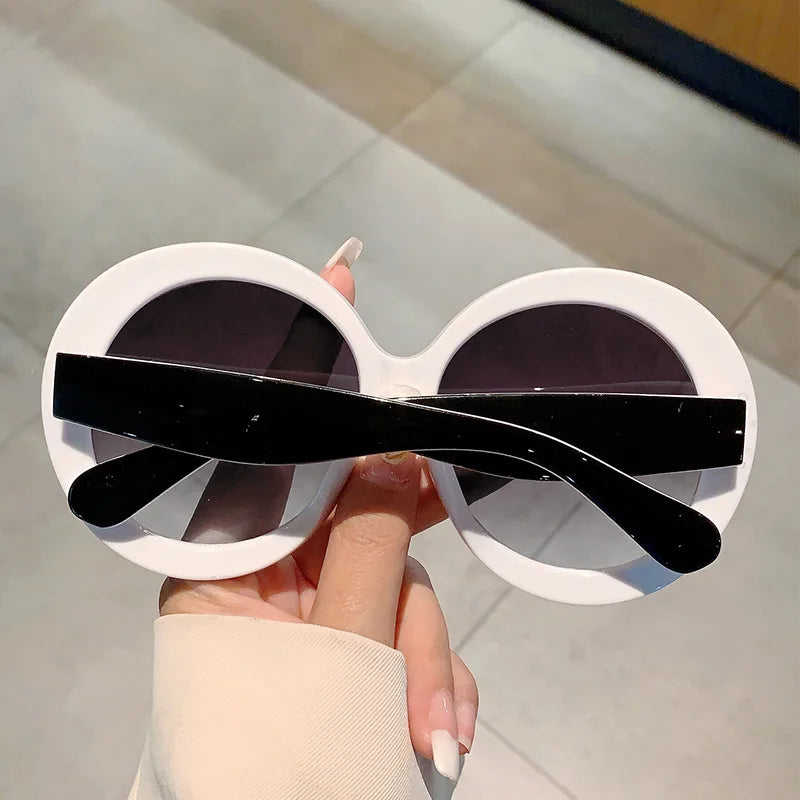 White Round-shaped sunglasses with black lenses held by a hand against a neutral background
