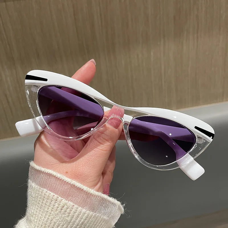 Hand holding a pair of cat-eye sunglasses with white frame and purple lenses against a neutral background.