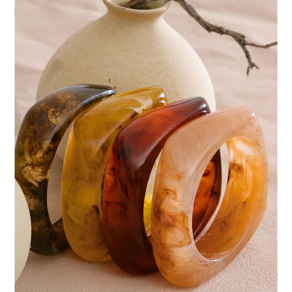 Set of four marbled bangles in front of a ceramic vase on a neutral background