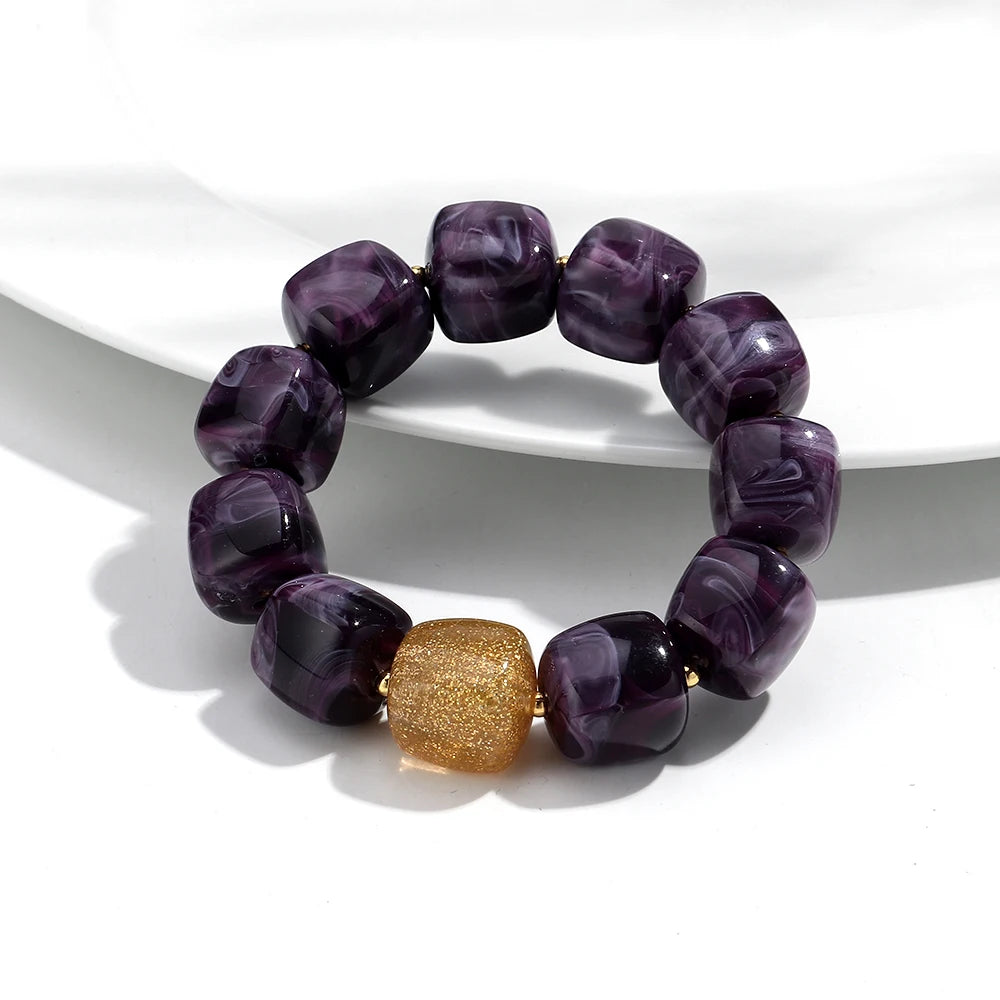 Purple beaded bracelet with a gold accent on a white surface