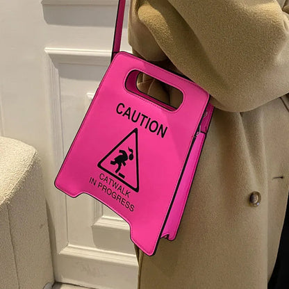 Person wearing a bright pink bag with a 'Caution: Catwalk in Progress' sign, standing against a white wall.