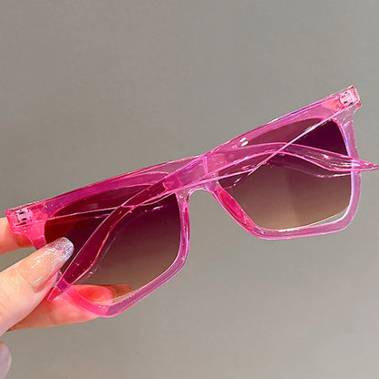 Pink sunglasses held by a hand against a gray background