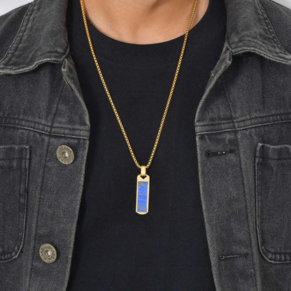 Person wearing a gold necklace with a blue pendant against a black shirt and denim jacket.