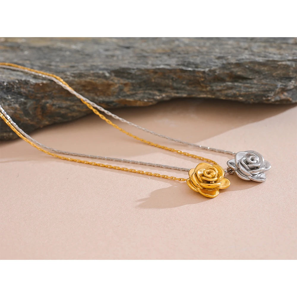 Two gold necklaces with floral pendants on a stone surface