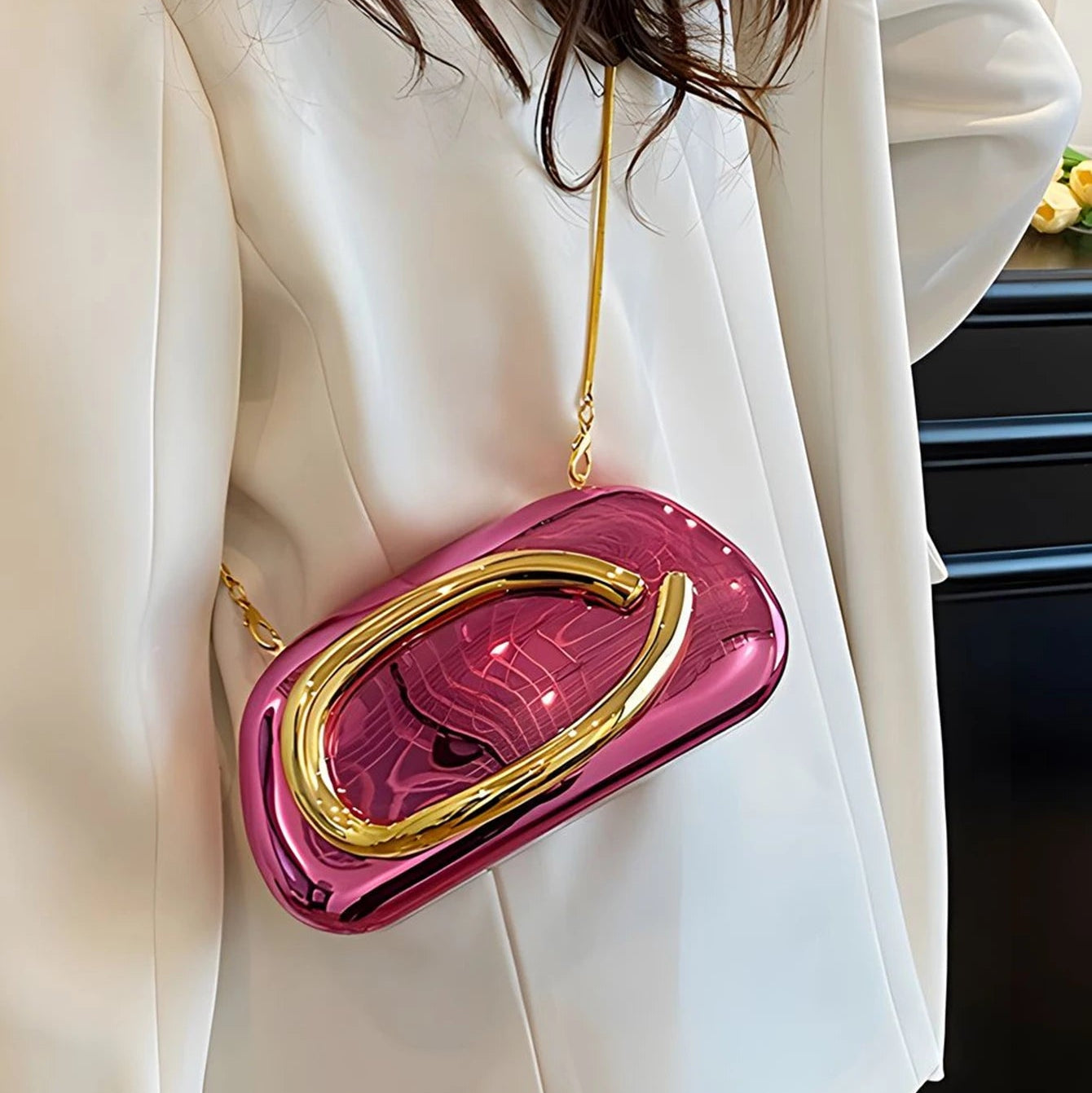 Pink and gold handbag worn by a person in a white outfit.